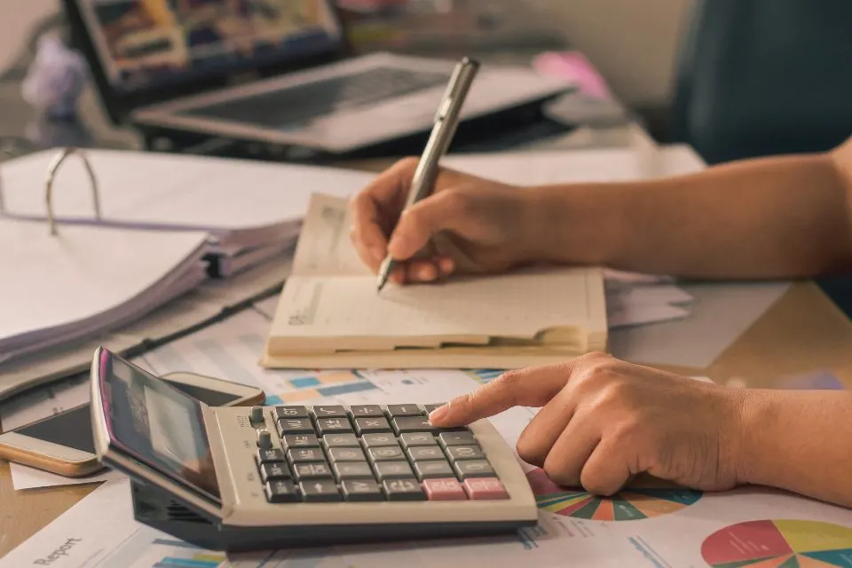 Pessoa fazendo contas numa calculadora sobre papéis e gráficos